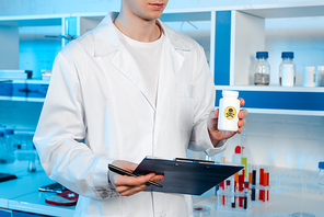 cropped view of scientist holding clipboard and bottle with toxic symbol