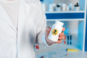 cropped view of scientist holding bottle with toxic symbol