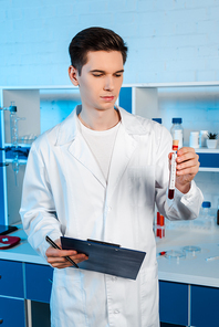 handsome scientist holding test tube with coronavirus lettering and clipboard