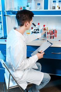 scientist in white coat holding clipboard and touching test tube