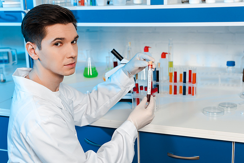 handsome scientist in latex gloves holding sample with coronavirus lettering