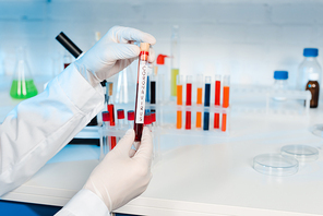 cropped view of scientist in latex gloves holding sample with coronavirus lettering