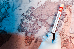 cropped view of scientist holding test tube with coronavirus lettering near map