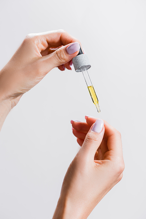 cropped view of woman applying oil from pipette on fingernails isolated on grey