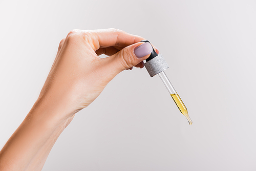 cropped view of woman holding pipette with oil isolated on grey