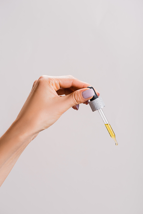 cropped view of woman holding pipette with oil isolated on grey