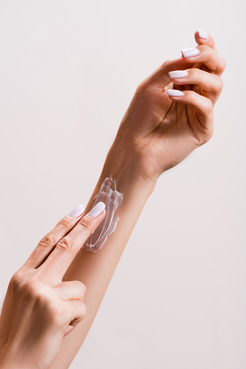 cropped view of woman applying hand cream on arm isolated on grey