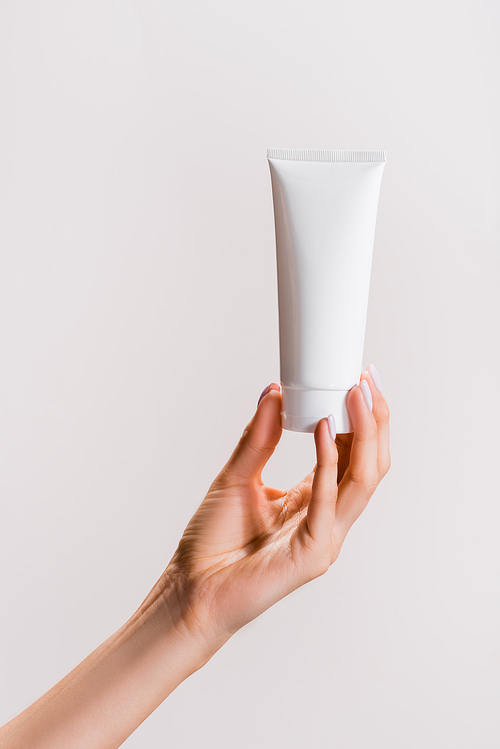 cropped view of woman holding tube of hand cream isolated on grey