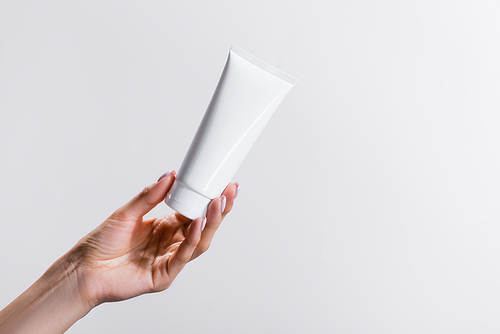 cropped view of woman holding tube of hand cream isolated on grey