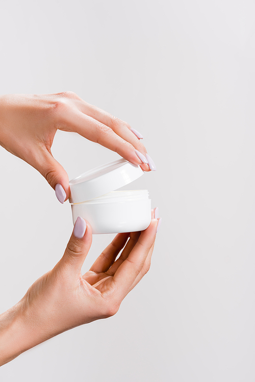 cropped view of woman opening container of hand cream isolated on grey