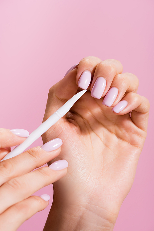 cropped view of woman using cuticle pusher isolated on pink