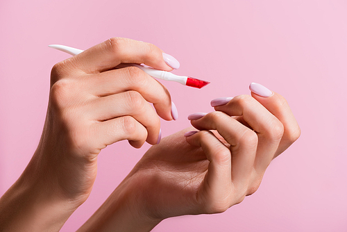 cropped view of woman using cuticle pusher isolated on pink