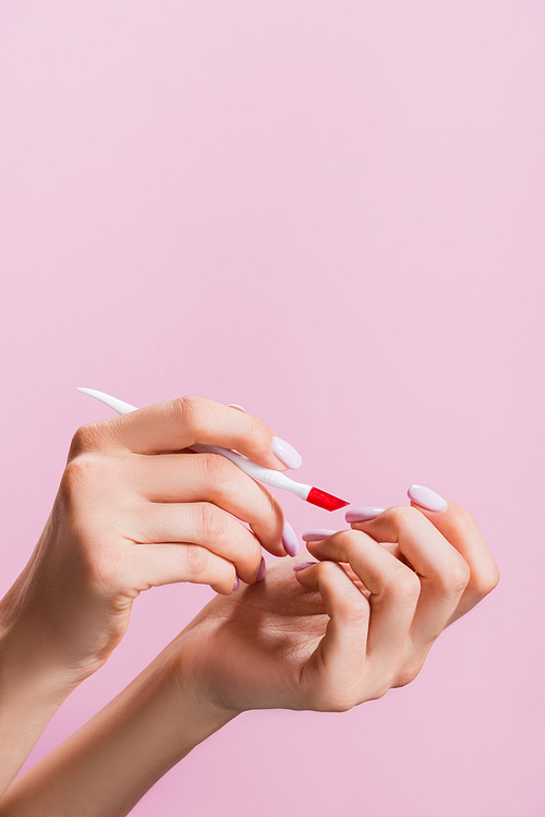 cropped view of woman using cuticle pusher isolated on pink