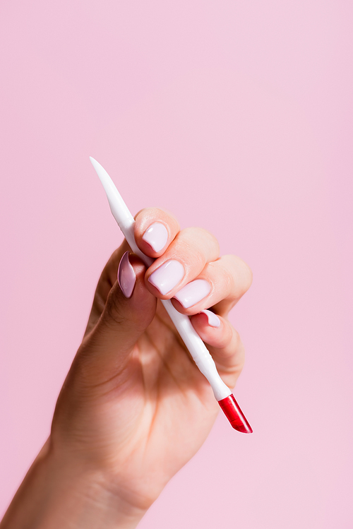 cropped view of woman holding cuticle pusher isolated on pink