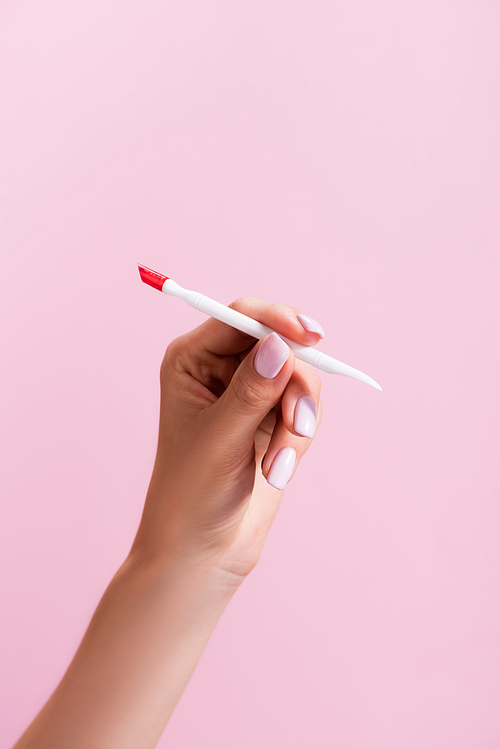 cropped view of woman holding cuticle pusher isolated on pink