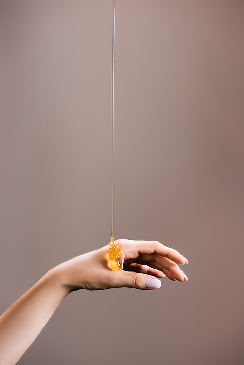 cropped view of female hand in honey isolated on grey