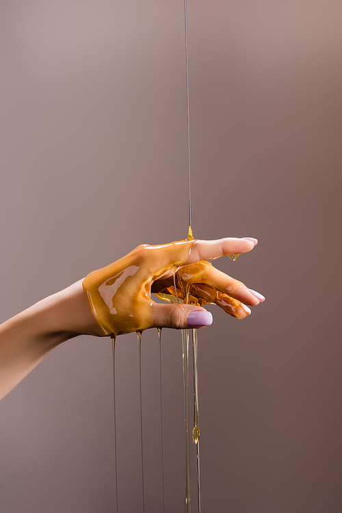 cropped view of female hand in honey isolated on grey