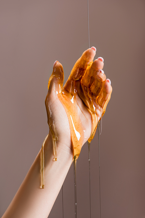 cropped view of female hand in honey isolated on grey