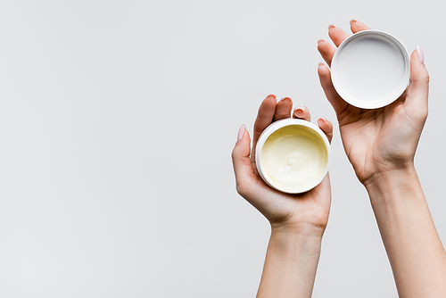 top view of woman holding jars with cosmetic cream isolated on white