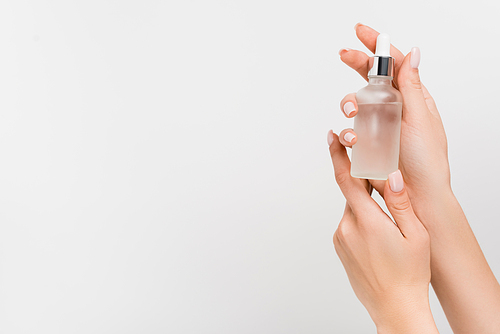 cropped view of woman holding bottle with serum in hands isolated on white