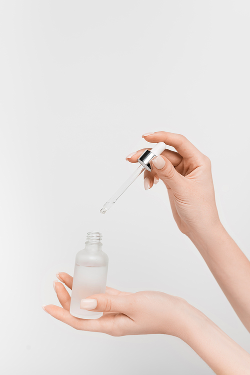 partial view of woman holding bottle with serum and pipette isolated on white
