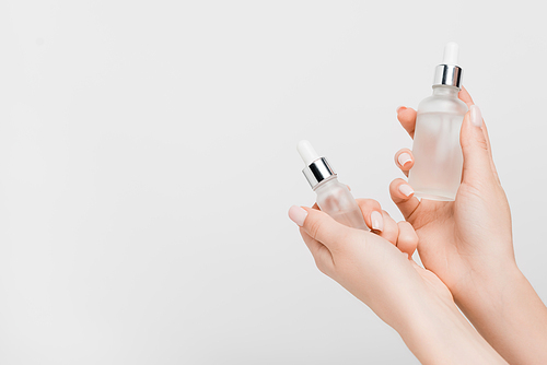 cropped view of woman holding bottles with serum in hands isolated on white