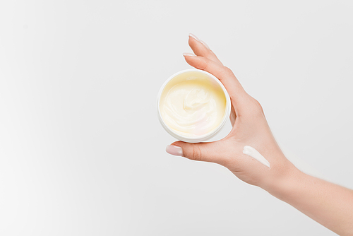 partial view of woman holding container with cosmetic cream in hand isolated on white