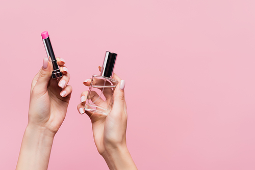 cropped view of woman holding lipstick and bottle with perfume isolated on pink