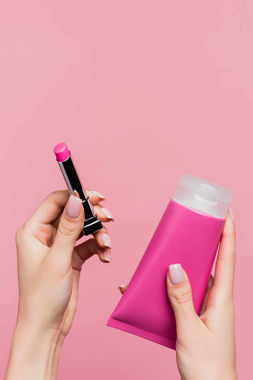 cropped view of woman holding lipstick and tube with body cream isolated on pink