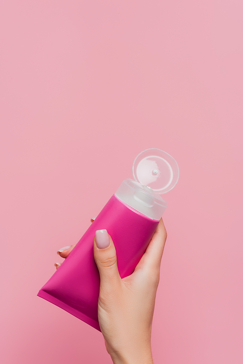 partial view of woman holding tube with lotion in hand isolated on pink