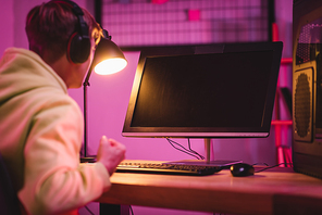 Computer monitor with blank screen near gamer in headset showing yeah gesture on blurred foreground