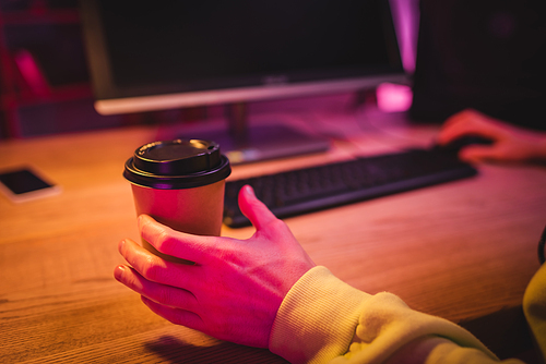 Cropped view of man taking coffee to go while playing video game on computer on blurred background