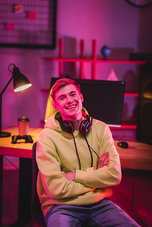 Smiling gamer in headphones  while sitting near computer and gamepad on blurred background
