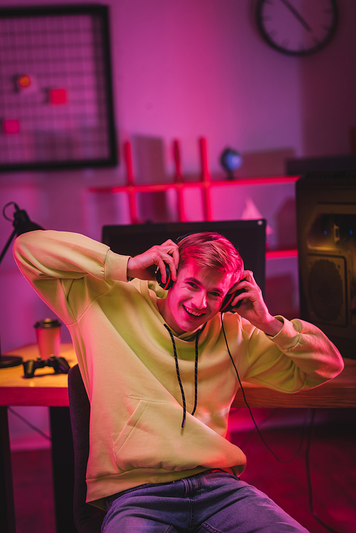 Cheerful gamer holding headphones near computer and joystick on blurred background