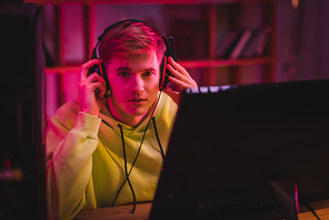 Young gamer holding headphones and  near computer monitor on blurred foreground