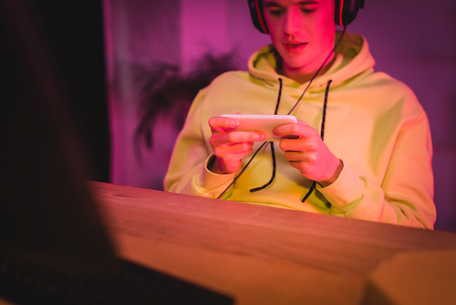 Smartphone in hands of gamer in headphones on blurred background