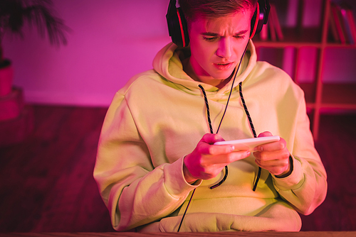 Worried gamer in headphones using smartphone at home