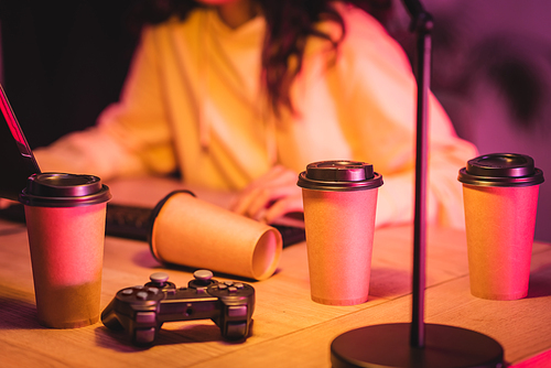 KYIV, UKRAINE - AUGUST 21, 2020: Takeaway coffee and joystick near gamer and computer on blurred background