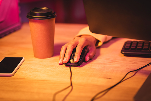 Cropped view of gamer using computer mouse near smartphone with blank screen and coffee to go