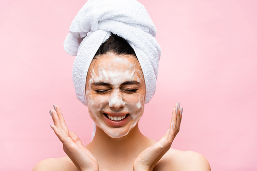 smiling beautiful woman with towel on hair and foam on face isolated on pink