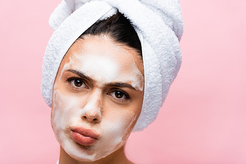 beautiful woman with towel on hair and foam on face grimacing isolated on pink