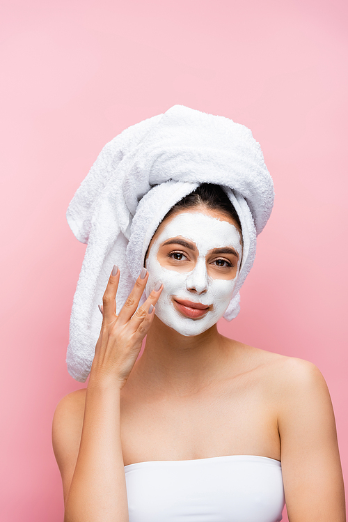 smiling beautiful woman with towel on head and clay mask on face isolated on pink
