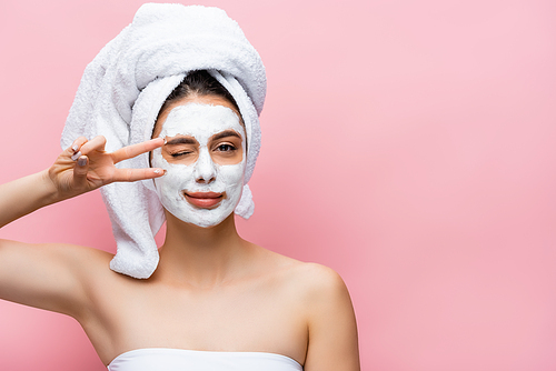 beautiful woman with towel on head and clay mask on face grimacing isolated on pink
