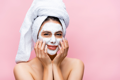 beautiful woman with towel on head and clay mask on face isolated on pink