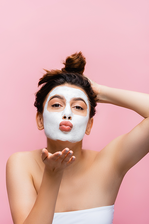 beautiful woman with clay mask on face blowing kiss isolated on pink