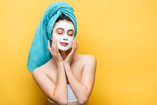 beautiful woman with closed eyes, blue towel on hair and clay mask on face isolated on yellow