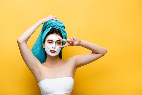 beautiful woman with blue towel on hair and clay mask on face grimacing isolated on yellow