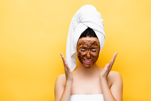 beautiful woman with towel on head and coffee mask on face isolated on yellow