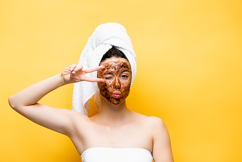 beautiful woman with towel on head and coffee mask on face grimacing isolated on yellow