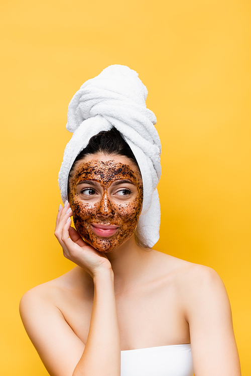 beautiful woman with towel on head and coffee mask on face isolated on yellow